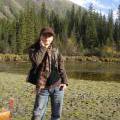 Yuan Ping stands outside in front of tall pine trees.