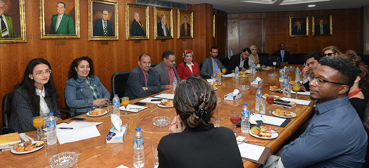 A group of people have a discussion while sitting at a long table and eating lunch.