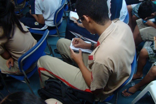 A person sits in a chair and writes down notes in a notepad.