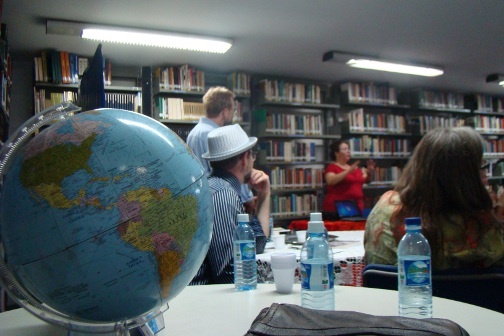 A group of people sit around a room and listen to someone present.