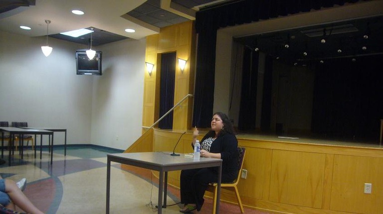 BTL guest lecturer and Arab-American author Randa Jarrar reads from her work while sitting at a desk before an audience.