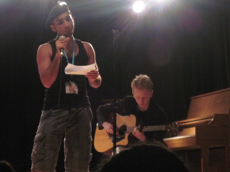 Two Between the Lines participants perform at a talent show.  One speaks into a microphone and the other plays a guitar.