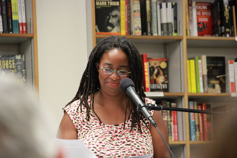 Camille T. Dungy does a reading a Prairie Lights.  Bookshelves can be seen behind her.