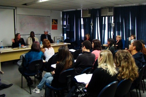 Three people sit at a table and present in front of a classroom full of people.