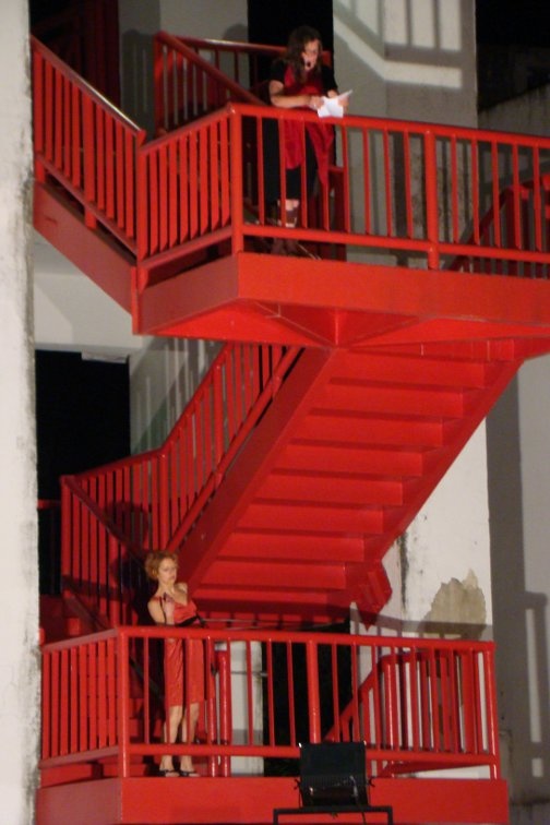 Two people stand on a bright red staircase, speaking to an audience.