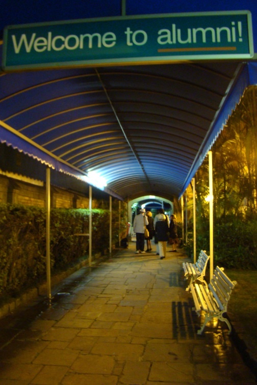 A group of people walk under a sign that reads "Welcome to Alumni!"