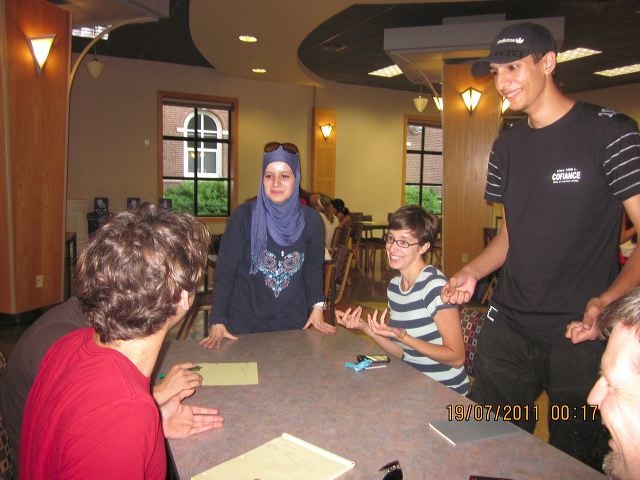 A group of students sit at a table and learn Arabic.