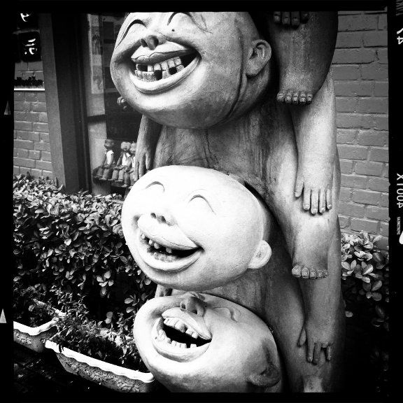 A wooden statue of three children sitting atop each others shoulders.