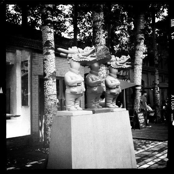 Public art in Beijing's 798 Art Zone - three statues on a concrete podium with the bodies of humans and heads of dragons.