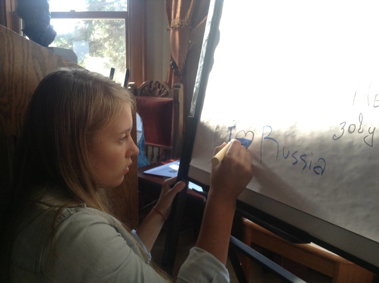 Between the Line participant Alina writes " I heart Russia" on a whiteboard.