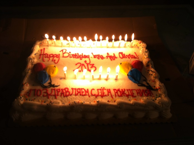 A birthday cake that reads "Happy Birthday Inna and Olivia" in English and Russian with lit candles.