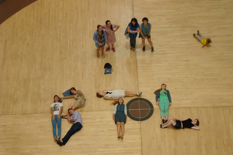 A group of Between the Lines participants spell "BTL" by laying on a gymnasium floor.