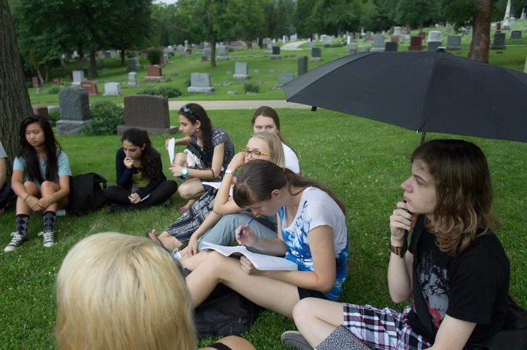 A group of Between the Lines participants sit in a circle at a cemetary, with headstones in the background.