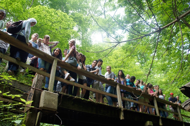 A group of Between the Lines participants pose for a picture on a wooden bridge in the woods.