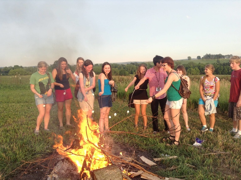 A group of Between the Lines participants gather around a fire to roast marshmellows.