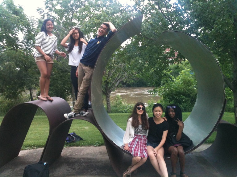 A group of Between the Lines participants pose together on a sculpture in a park.