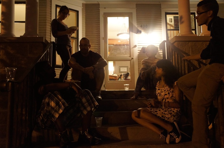 A group of Between the Lines participants sit outside Shambaugh house eating pizza at night.