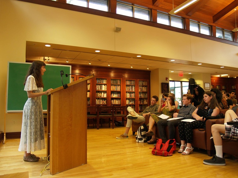 A person reads from a podium in front of an audience.