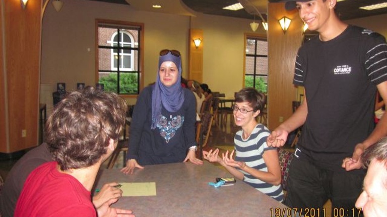 A group of students sit at a table and learn Arabic.
